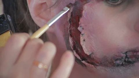 Makeup artist makes wax plastic makeup in form of bloody wound on face of girl Stock Footage 105600037