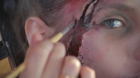 Makeup artist makes wax plastic makeup in form of bloody wound on face of girl Stock Footage 105600039