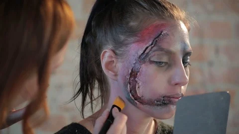 Makeup artist makes wax plastic makeup in form of bloody wound on face of girl Stock Footage 105600041