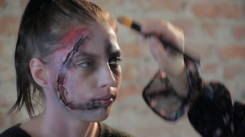 Makeup artist makes wax plastic makeup in form of bloody wound on face of girl Stock Footage 105600059