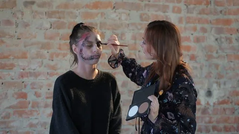 Makeup artist makes wax plastic makeup in form of bloody wound on face of girl Stock Footage 105600068