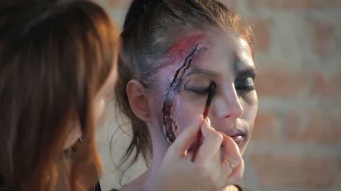 Makeup artist makes wax plastic makeup in form of bloody wound on face of girl Video stock 105600076