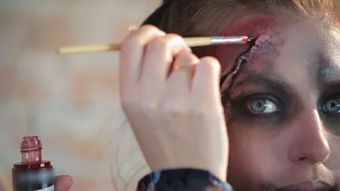 Makeup artist makes wax plastic makeup in form of bloody wound on face of girl Stock Footage 105600103