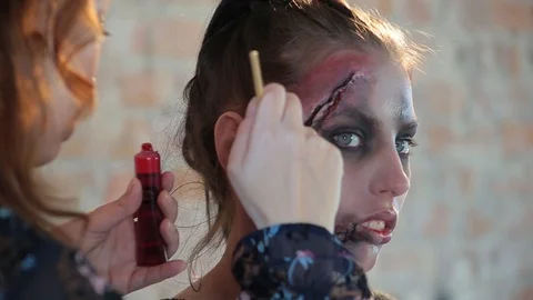 Makeup artist makes wax plastic makeup in form of bloody wound on face of girl Stock Footage 105600128