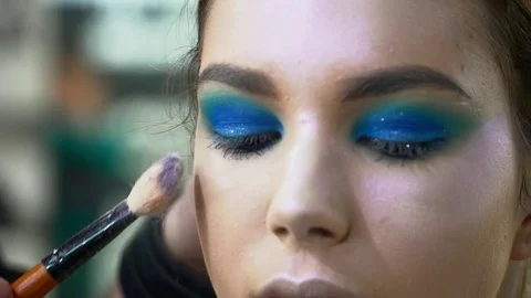 Makeup artist making beautiful face art for a young woman with makeup brush Stock Footage 76572626