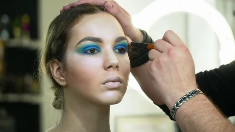 Makeup artist making beautiful face art for a young brunette woman with makeup Stock Footage 76573103