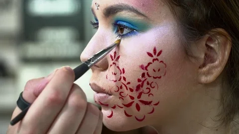 Makeup artist making beautiful face art with a stencil with red flowers Stock Footage 76574214