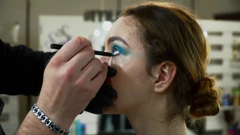 Makeup artist making the face art with blue shadows for a young woman Stock Footage 76570974