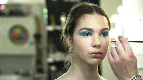 Makeup artist making the face art with blue shadows for a young woman closeup Stock Footage 76571074