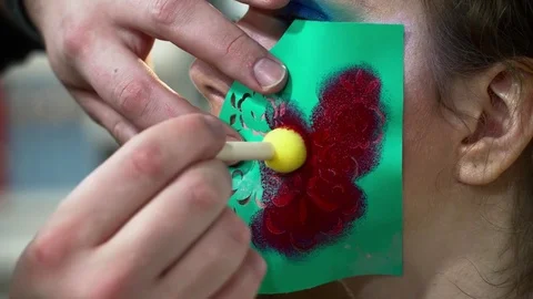 Makeup artist making face art with a stencil with flowers closeup Stock Footage 76573666