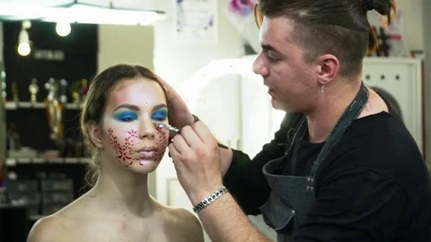 Makeup artist making face art with a stencil with red flowers in front of the Stock Footage 76574298