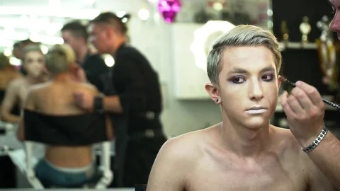 Makeup artist making face art for a young blonde man in the makeup studio Stock Footage 76579517