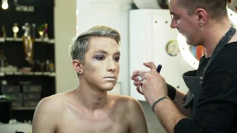 Makeup artist making face art for a young blonde man with a makeup brush Stock Footage 76579822