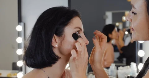Makeup artist patches under the model’s eyes, brunette girls on face Stock Footage 124781267