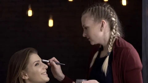 Makeup artist puts eye shadow on face model and laughs Vídeo Stock 85757439