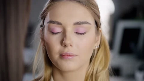 The makeup artist uses a brush to apply pink eyeshadow to the model's eyelids Stock Footage 236399551