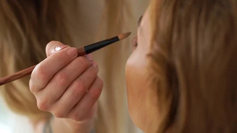 Makeup artist using cosmetic brush for makeup application to woman face in Video stock 91473809