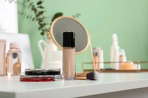 Makeup brush and different cosmetics on table near green wall in room, closeu Stock Photos