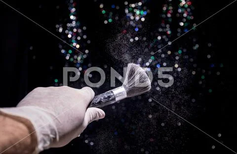 Makeup brush in hand with cosmetic powder on dark background with light and s Stock Photos