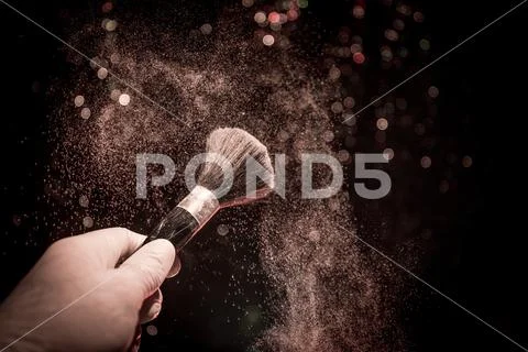 Makeup brush in hand with cosmetic powder on dark background with light and s Stock Photos