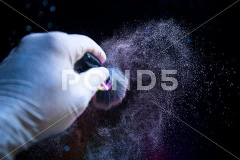 Makeup brush in hand with cosmetic powder on dark background with light and s Stock Photos