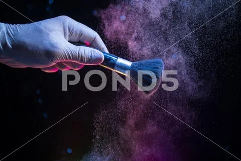 Makeup brush in hand with cosmetic powder on dark background with light and s Stock Photos
