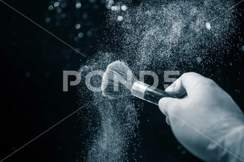 Makeup brush in hand with cosmetic powder on dark background with light and s Stock Photos
