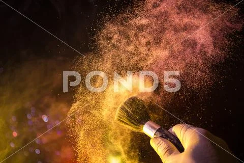 Makeup brush in hand with cosmetic powder on dark background with light and s Stock Photos