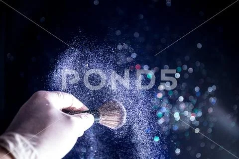 Makeup brush in hand with cosmetic powder on dark background with light and s Stock Photos