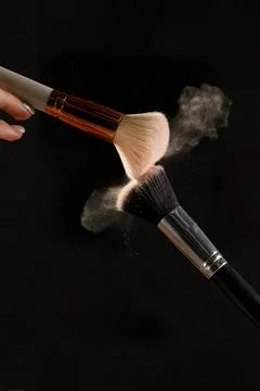 Makeup brushes in action with powder dust on a black background Stock Photos