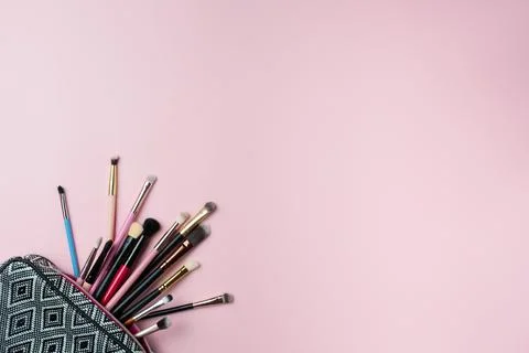 Makeup brushes falling out of cosmetics on pink background Stock Photos