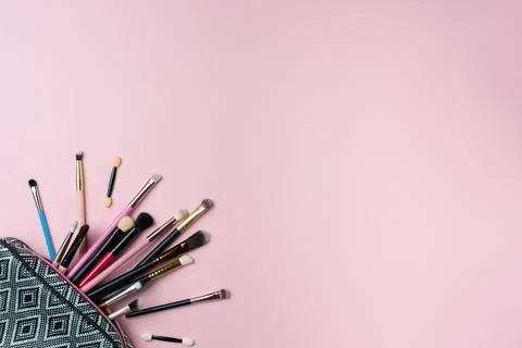Makeup brushes falling out of cosmetics on pink background Stock Photos