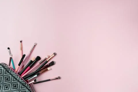 Makeup brushes falling out of cosmetics on pink background Foto stock