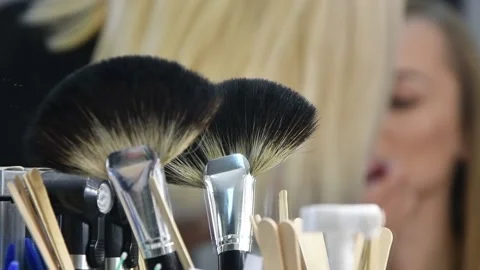 Makeup brushes in the foreground, in the background, a makeup artist paints the  Video stock 143505152