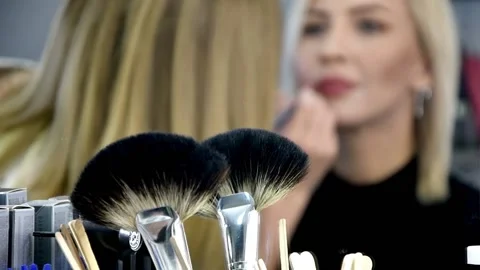 Makeup brushes in the foreground, in the background, a makeup artist paints the  Stock Footage 143505933