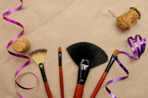Makeup brushes lie on craft paper with holiday ribbon and champagne cork Stock Photos