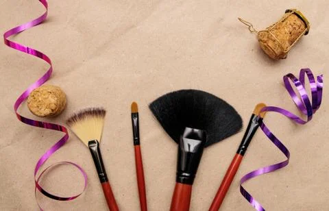 Makeup brushes lie on craft paper with holiday ribbon and champagne cork Stock Photos