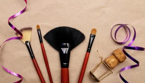 Makeup brushes lie on craft paper with holiday ribbon and champagne cork Stock Photos