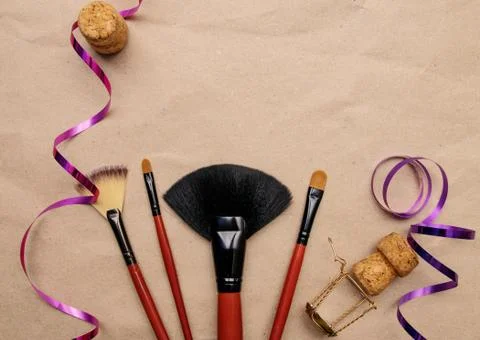 Makeup brushes lie on craft paper with holiday ribbon and champagne cork Stock Photos
