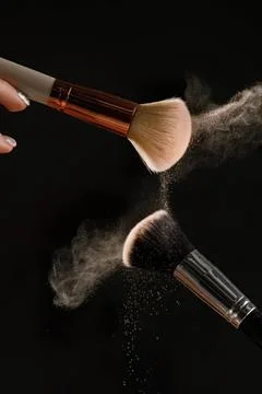Makeup brushes with powder flying in dark background Stock Photos