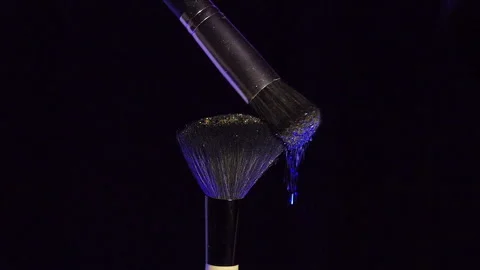 Makeup brushes touch each other on dark background and small particles of Stock Footage 228817362