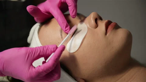 Makeup Concept. The Master of Eyelash Extension in Pink Gloves Lengthens Stock Footage 107382431
