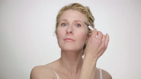 Makeup Demonstration: Beautiful blonde uses eyebrow brush looking in mirror Video stock 193832310