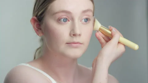 Makeup demonstration: ￼Caucasian blonde model in studio applies blush with brush Stock Footage 193940145