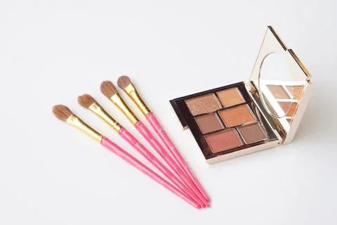 A makeup eyeshadow palette with warm neutral tones and four pink handled makeup  Stock Photos