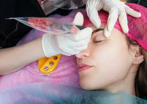 Makeup master makes eyebrow tattooing to client in salon. Close up of Stock Photos