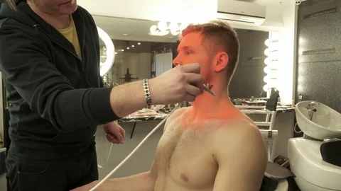 Makeup master sprays orange color to the model's face from aerograph Stock Footage 73519103