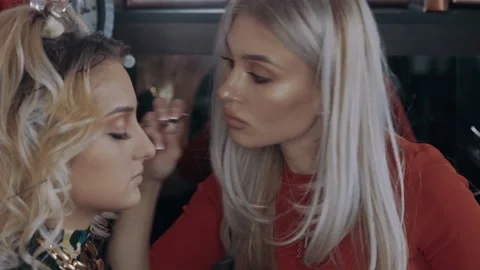 The makeup professional applies false eyelashes to the charismatic blonde woman Stock Footage 157457484