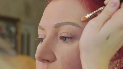 Makeup stylist makes beautiful eyebrows to young redhead woman at beauty shop Stock Footage 82677026