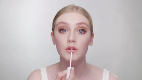 Makeup Tutorial: Attractive blonde model in white studio applies lip gloss Stock Footage 193705771